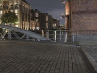 there is a bench sitting on the street with buildings in the background at night and street light