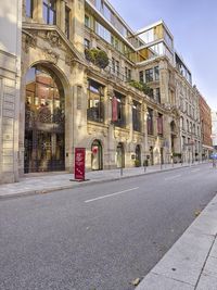 an empty street lined with buildings next to an empty city sidewalk at sunset light,