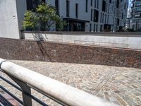 a brick walkway next to a tall building and a railing with black railing rails and railing posts