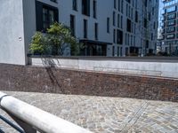 a brick walkway next to a tall building and a railing with black railing rails and railing posts