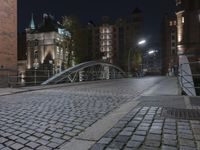 two people walking across a brick walkway in front of a cathedral at night with their bike