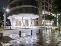 this is an empty street at night near a big building with a very light on the outside