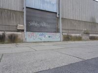 an empty cement sidewalk next to a building covered in graffiti paint and grafitti