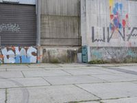 an empty cement sidewalk next to a building covered in graffiti paint and grafitti