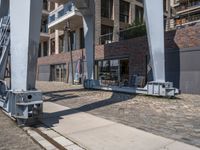 a train moving down the road under a bridge near buildings and a craner truck