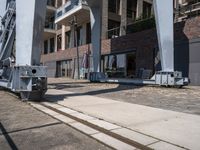 a train moving down the road under a bridge near buildings and a craner truck