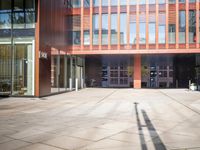 a long shadow of a person standing outside an office building with red glass on the facade and glass windows