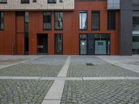 the stone driveway has some bricks on it and brick walls are brown and black, and two buildings have red doors