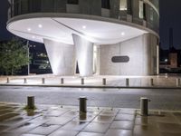 an image of the night time view of a modern building and street scene with some benches