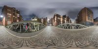 a 360 - ray view of buildings and street lights from a bridge over a cobblestone road