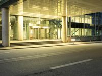 the outside of a building at night with cars parked on the sidewalk and lights on