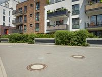 a building is surrounded by many greenery and a manholes on a paved sidewalk