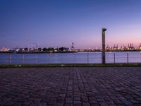 an empty bench sitting by the water with the view of the industrial landscape behind it