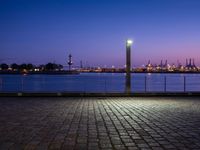 an empty bench sitting by the water with the view of the industrial landscape behind it