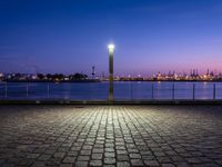 an empty bench sitting by the water with the view of the industrial landscape behind it