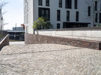 a brick walkway beside a stone wall leading down to a staircase with concrete steps leading to an apartment building