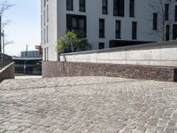 a brick walkway beside a stone wall leading down to a staircase with concrete steps leading to an apartment building