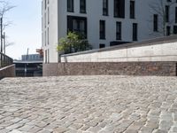 a brick walkway beside a stone wall leading down to a staircase with concrete steps leading to an apartment building