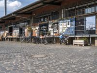 people with bicycles are walking on the cobblestones at an outdoor area with some tables and bars