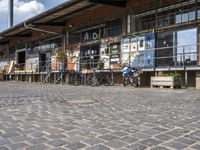 people with bicycles are walking on the cobblestones at an outdoor area with some tables and bars