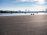 a man is sitting on a skateboard near the water and some dock equipment on the sidewalk