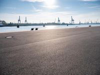 a man is sitting on a skateboard near the water and some dock equipment on the sidewalk