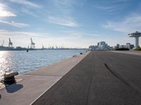 a dock next to a body of water near some buildings and cranes in the distance