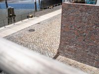 a brick wall with a brick walkway near a water front with people walking past it