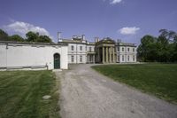 a graveled path leads to the front of a large white mansion that is next to a field