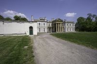 a graveled path leads to the front of a large white mansion that is next to a field