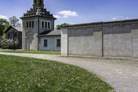 an old church is next to a wall and grassy field with daisies, in the country