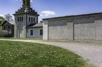 an old church is next to a wall and grassy field with daisies, in the country