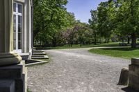 a gravel path and a bench in the shade of a tree, in front of a building