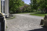 a gravel path and a bench in the shade of a tree, in front of a building