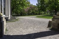 a gravel path and a bench in the shade of a tree, in front of a building