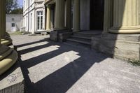 an old mansion entrance in the sunshine of day with many pillars and windows on either side of the front door