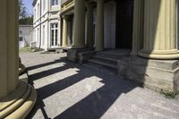 an old mansion entrance in the sunshine of day with many pillars and windows on either side of the front door