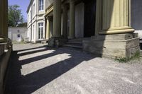 an old mansion entrance in the sunshine of day with many pillars and windows on either side of the front door