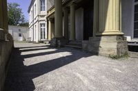 an old mansion entrance in the sunshine of day with many pillars and windows on either side of the front door