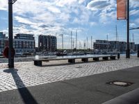 an empty bench next to a harbor with some boats on it and buildings in the background