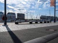 an empty bench next to a harbor with some boats on it and buildings in the background