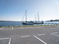 several boats and sailboats sit parked on the side of a parking lot at a harbor