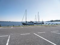 several boats and sailboats sit parked on the side of a parking lot at a harbor