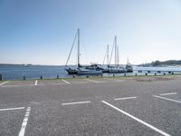 several boats and sailboats sit parked on the side of a parking lot at a harbor