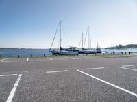 several boats and sailboats sit parked on the side of a parking lot at a harbor