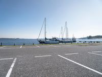 several boats and sailboats sit parked on the side of a parking lot at a harbor