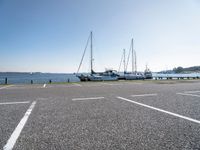 several boats and sailboats sit parked on the side of a parking lot at a harbor