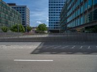 an empty parking lot with many buildings in the background on a sunny day by a fence