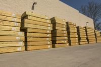 a bunch of yellow lumber boards on a building side lot in a parking lot next to trees