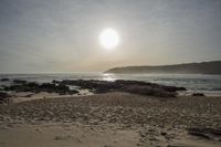 the sun sets on a hazy beach while the waves roll in to shore and shore